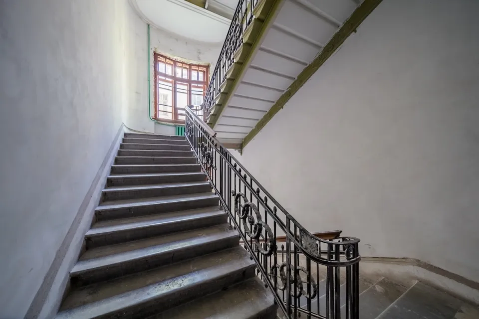 Wide apartment building staircase with curved wrought iron handrail.